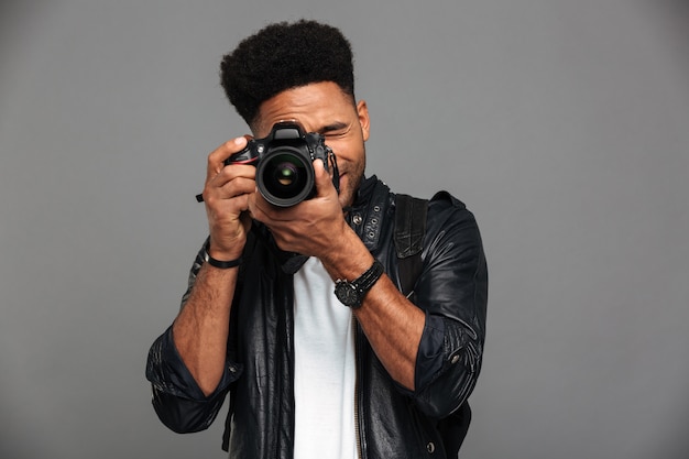 Handsome african guy with stylish haircut taking photo on digital camera