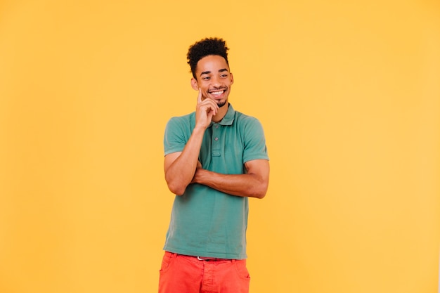 Handsome african man thinking about something with smile. Indoor shot of positive black guy expressing good emotions.