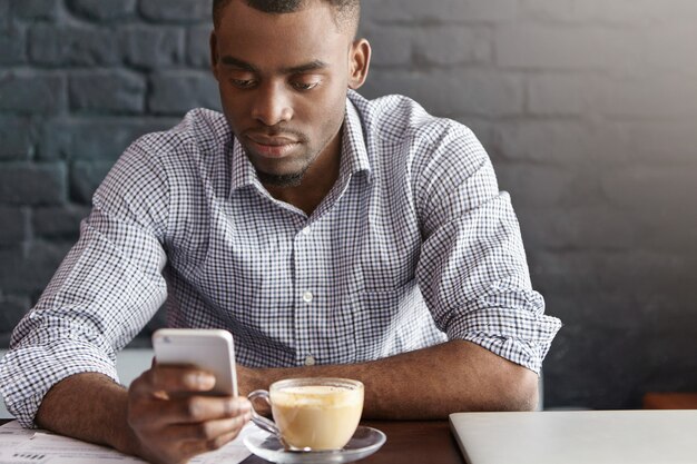 Handsome African office worker wearing checkered shirt with rolled up sleeves enjoying online communication