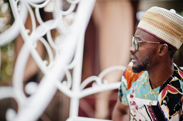 Handsome afro american man wearing traditional clothes cap and eyeglasses sitting at white carriage