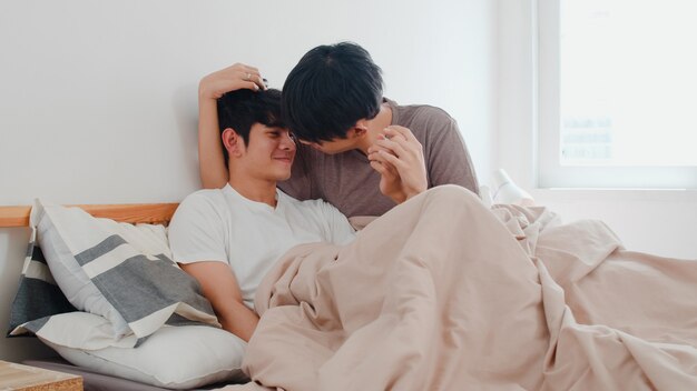 Handsome Asian gay couple talking on bed at home. Young Asian LGBTQ+ guy happy relax rest together spend romantic time after wake up in bedroom at modern house in the morning .