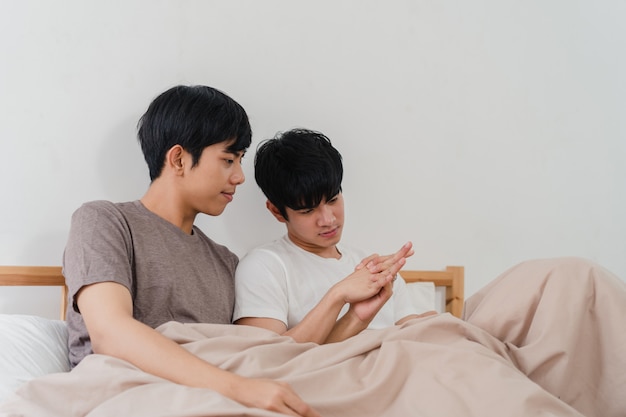 Handsome Asian gay couple talking on bed at home. Young Asian LGBTQ+ guy happy relax rest together spend romantic time after wake up in bedroom at modern house in the morning .