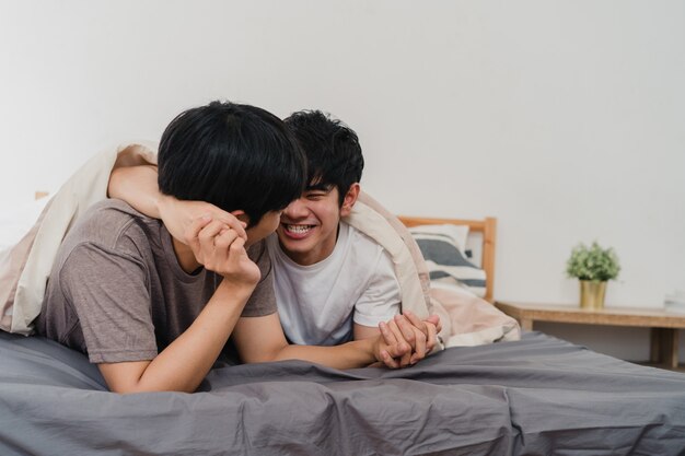 Handsome Asian gay couple talking on bed at home. Young Asian LGBTQ+ guy happy relax rest together spend romantic time after wake up in bedroom at modern house in the morning .