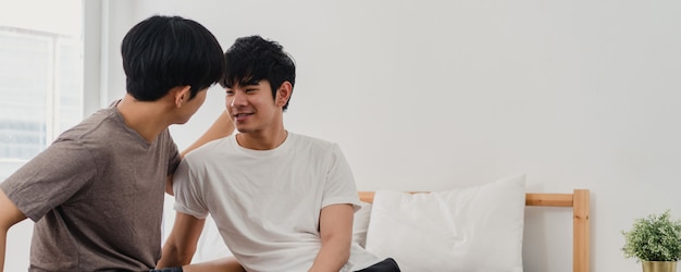Handsome Asian gay couple talking on bed at home. Young Asian LGBTQ+ guy happy relax rest together spend romantic time after wake up in bedroom at modern house in the morning .