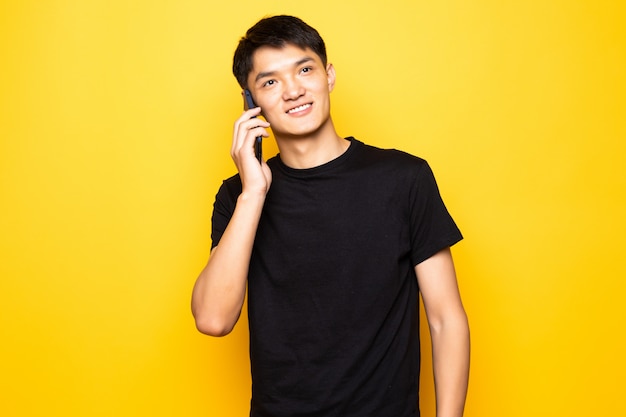 Handsome Asian young man talk on phone on yellow wall