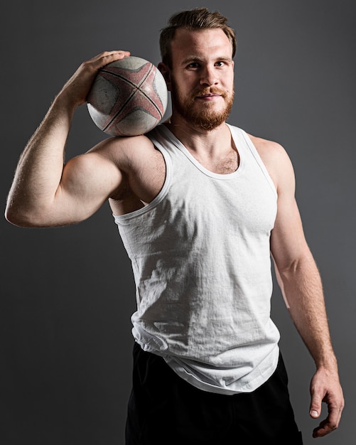 Handsome athletic male rugby player holding ball while posing