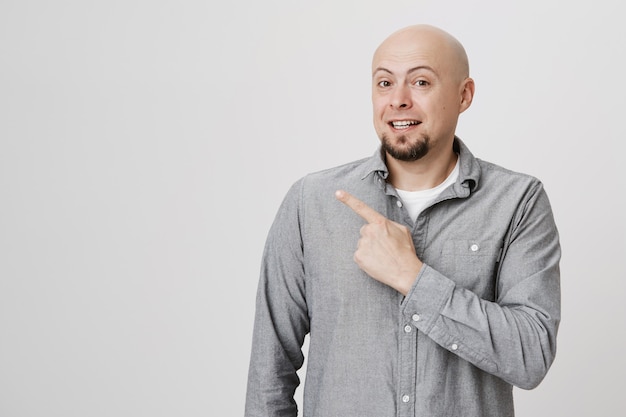 Free photo handsome bald adult man pointing upper left corner