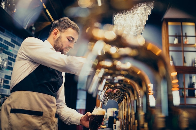 Handsome bartender pouring beer in pub