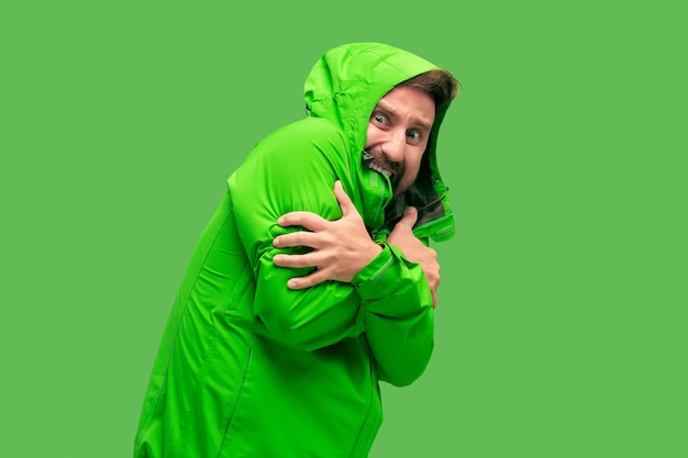 Handsome bearded freezing young man isolated on vivid trendy green color at studio. concept of the onset of autumn and cold