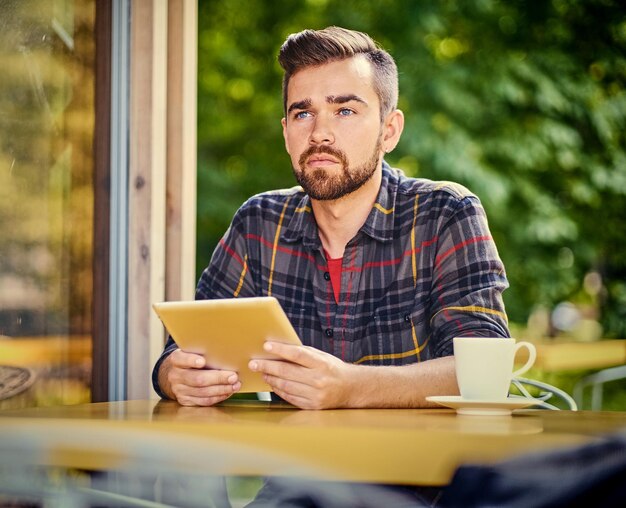 カフェでラップトップを使用してハンサムなひげを生やしたヒップスターの男性。