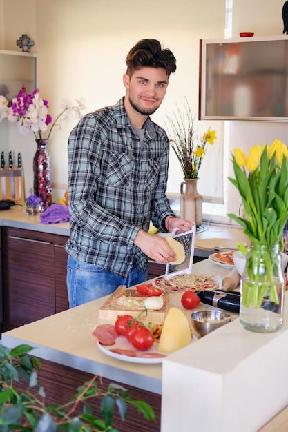 Красивый бородатый мужчина, одетый в флисовую рубашку, готовит салат из овощей на домашней кухне.