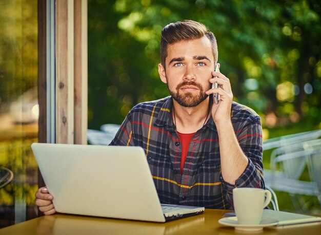 Handsome bearded male drinks coffee while using a laptop in a cafe.