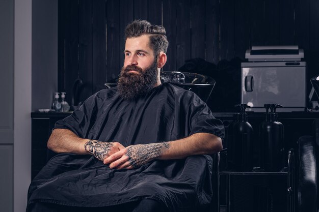 Handsome bearded male with a tattoo on his arms before hair wash in a hairdressers salon.