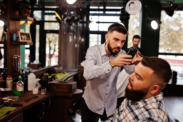 Free photo handsome bearded man at the barbershop barber at work making photo on his phone