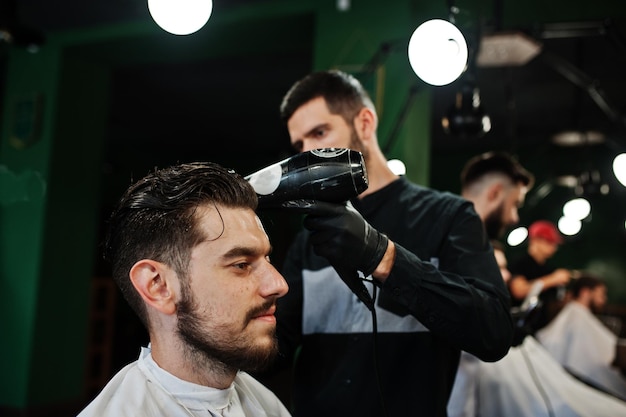 Handsome bearded man at the barbershop barber at work using hair dryer