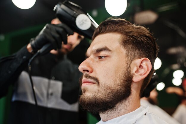 Красивый бородатый мужчина в парикмахерской парикмахер на работе с помощью фена