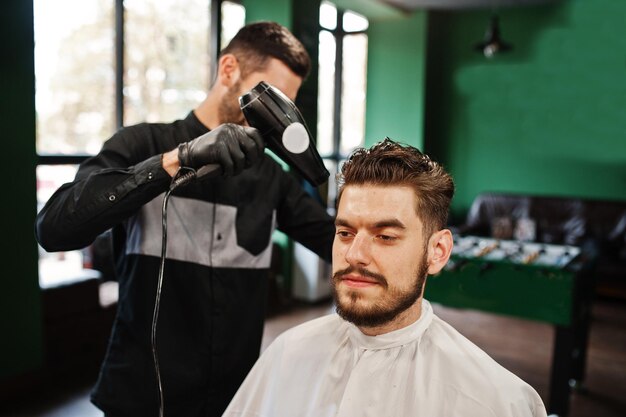 Handsome bearded man at the barbershop barber at work using hair dryer