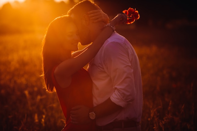 Handsome bearded man hugs woman in red dress tender standing in golden summer field