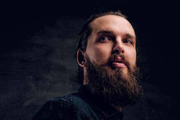 Handsome bearded man is posing for photographer at dark photo studio.