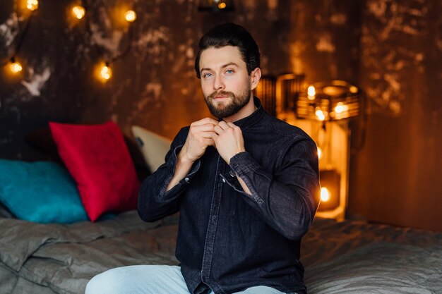 Handsome bearded man in morning time, sitting on his bed at modern badroom and dress up.