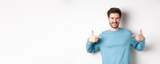 Бесплатное фото Красивый бородатый мужчина, указывающий пальцем на центр, саморекламирующий и выглядящий уверенно стоящим над белым