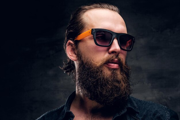 Красивый бородатый мужчина в солнцезащитных очках позирует фотографу в темной фотостудии.
