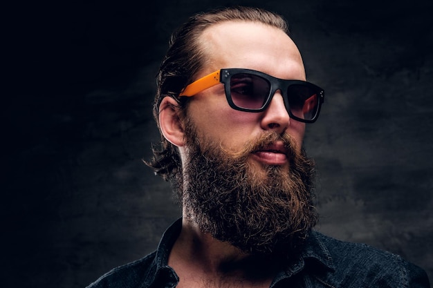 Handsome bearded man in sunglasses is posing for photographer at dark photo studio.