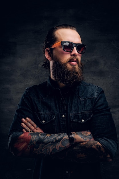 Free photo handsome bearded man in sunglasses is posing for photographer at dark photo studio.