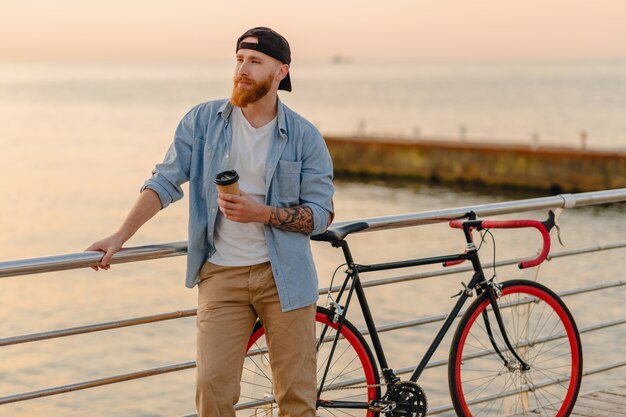 커피를 마시는 바다로 아침 일출에 자전거로 여행하는 잘 생긴 수염 난 남자, 건강한 활동적인 라이프 스타일 여행자