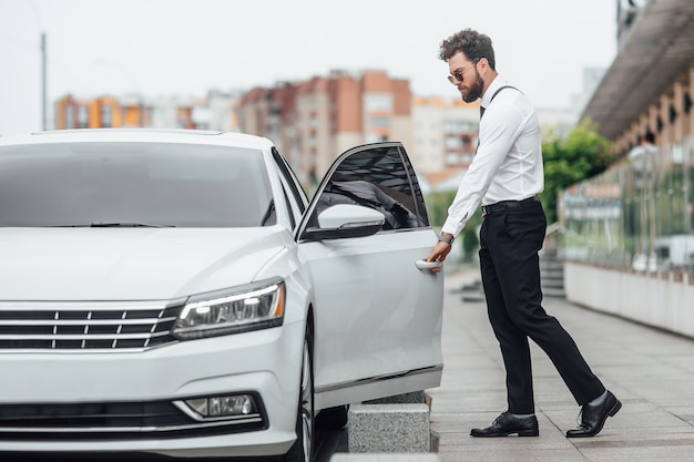 Handsome bearded manager entering his car while standing outdoors on the streets of the city near the modern office center