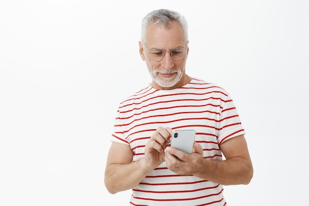 Handsome bearded old man using smartphone, texting message