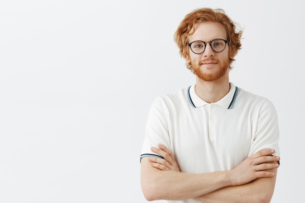 Free photo handsome bearded redhead guy posing against the white wall with glasses