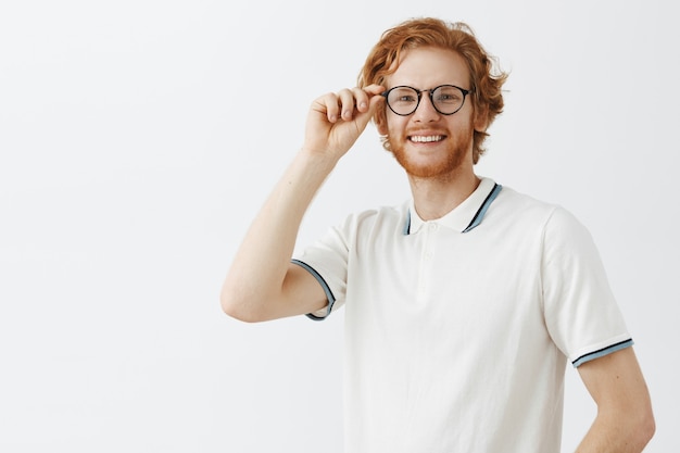 Free photo handsome bearded redhead guy posing against the white wall with glasses