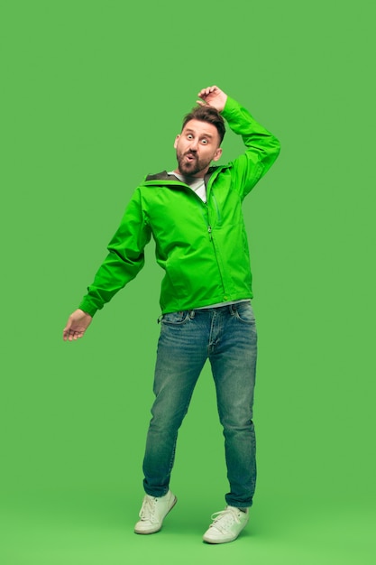 Handsome bearded smiling happy young man looking at camera isolated on vivid trendy green studio. concept of the autumn and cold time