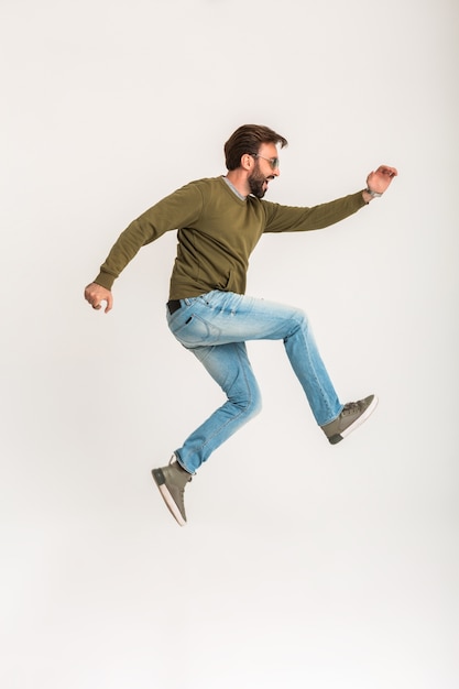 Free photo handsome bearded stylish man jumping running isolated dressed in sweatshirt, wearing jeans and sunglasses