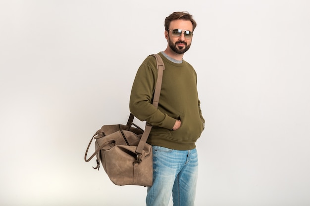 Free photo handsome bearded stylish man posing isolated dressed in sweatshirt with travel bag, wearing jeans and sunglasses