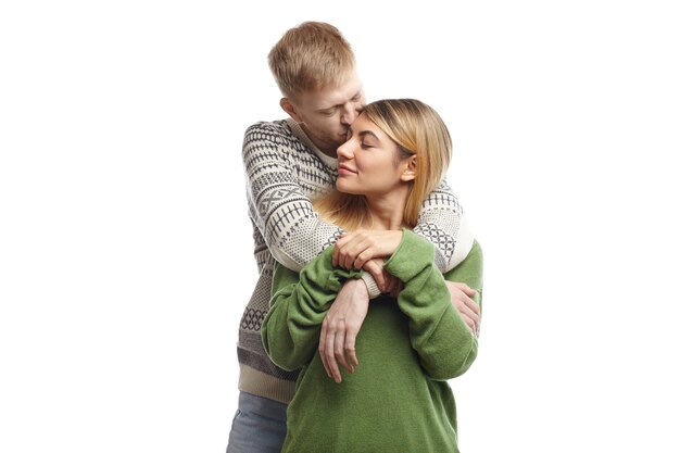 Handsome bearded young male hugging his cute girlfriend and kissing her on forehead, expressing his love and tenderness. Beautiful couple cuddling after long separation, keeping eyes closed