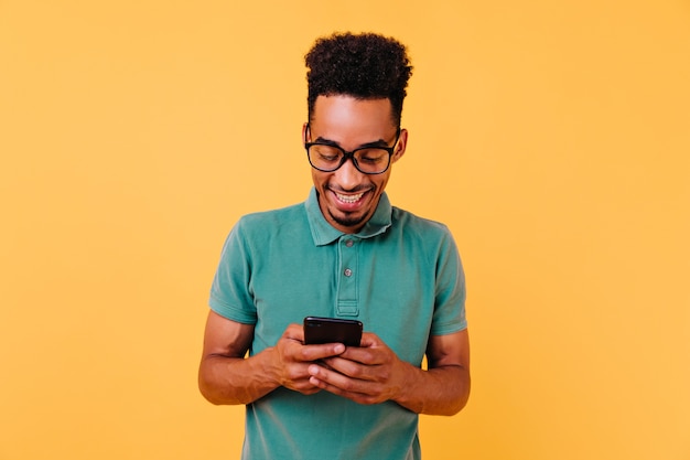 Handsome black guy in big glasses reading phone message. Portrait of pleased african man holding smartphone.