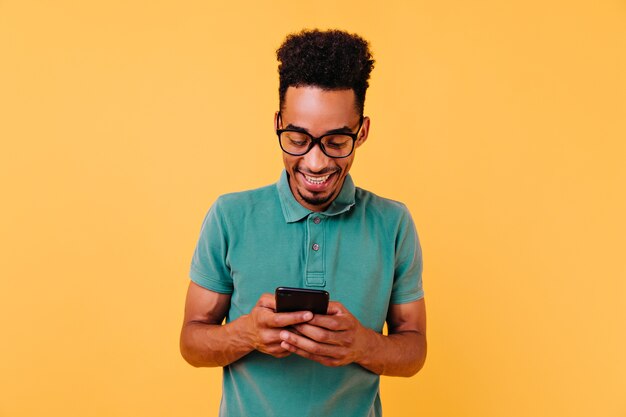 Handsome black guy in big glasses reading phone message. Portrait of pleased african man holding smartphone.