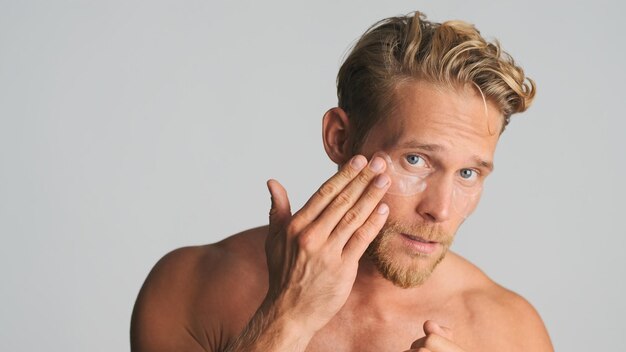 Handsome blond bearded man applying eye patches take care of his skin isolated on white background