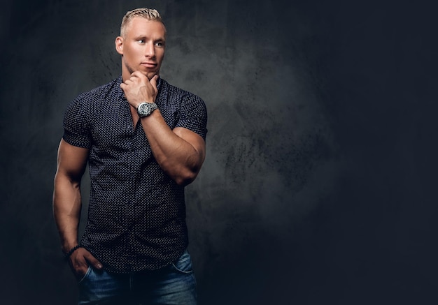 Handsome blond man in a dark blue shirt posing over grey background in a studio.