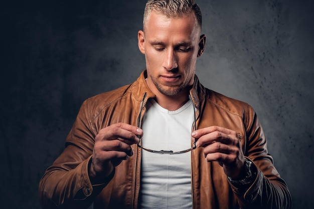 Handsome blond, muscular male in sunglasses, dressed in a white t shirt and brown leather jacket.