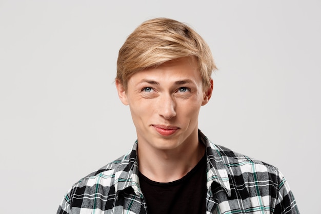  handsome blond young man wearing casual plaid shirt looking away on grey wall