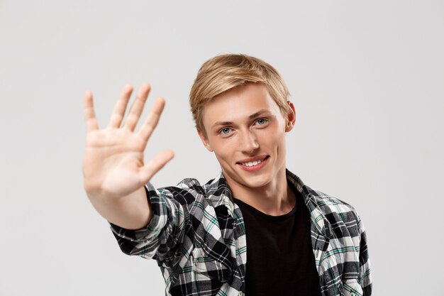 Handsome blond young man wearing casual plaid shirt showing open hand over grey wall