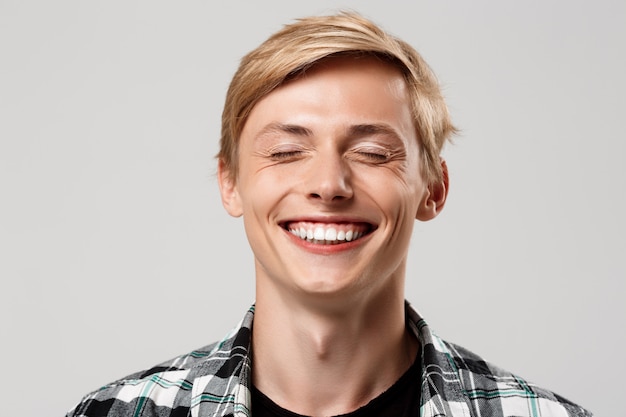  handsome blond young man wearing casual plaid shirt smiling with eyes closed on grey wall