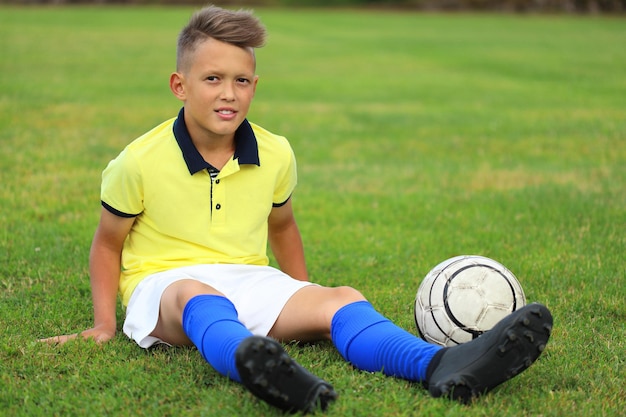 Красивый мальчик-футболист сидит на футбольном поле