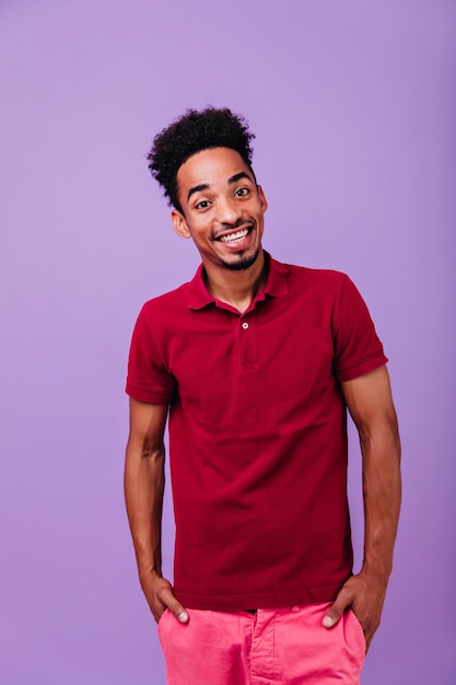 Handsome brunette man standing with hands in pockets. Indoor portrait of laughing optimistic african boy.