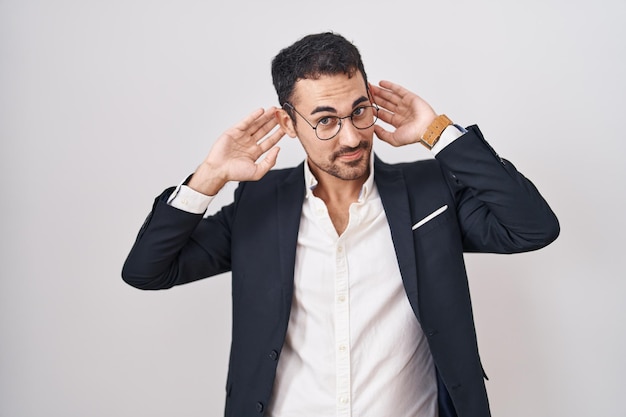 Handsome business hispanic man standing over white background smiling pulling ears with fingers funny gesture audition problem