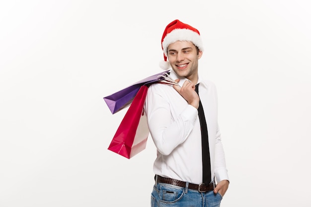 ハンサムなビジネスマンは、ショッピングバッグとサンタの帽子をかぶってメリークリスマスを祝います。