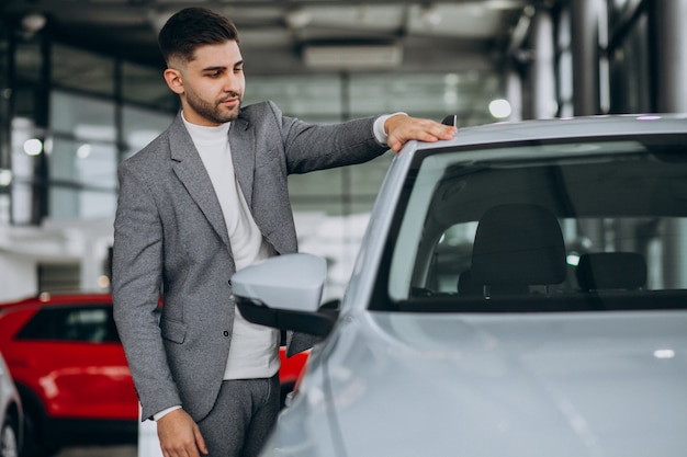 Uomo bello di affari che sceglie un'automobile in una sala d'esposizione dell'automobile